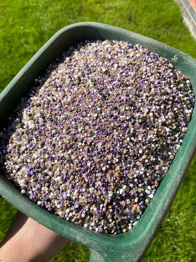 This image is a close up of a hand held lawn fertiliser spreader containing a granular fertiliser as part of our lawn services