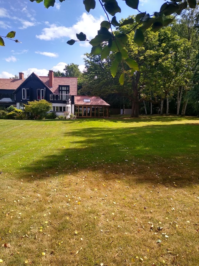 This image is of a large lawn during the summer months which benefits from lawn care services. The house can be seen in the distanced with the near area brown rather than green at the time