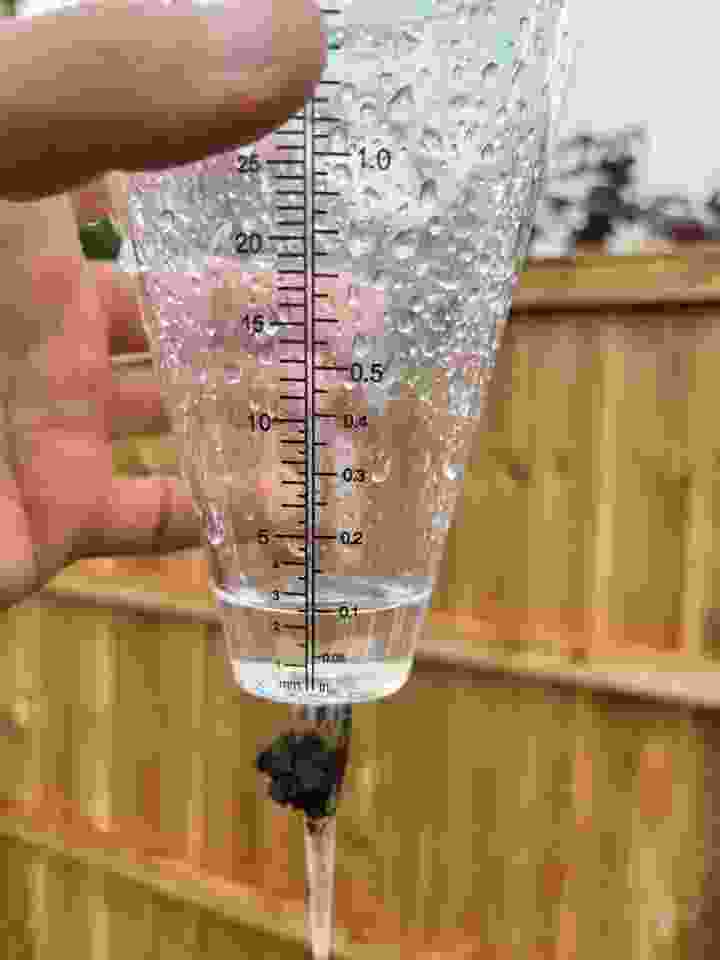 A rain gauge being held up following a light rain shower | Kingsbury Lawn Care